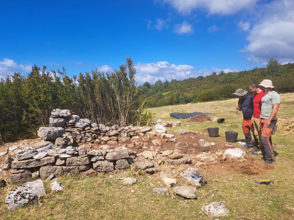 Colour photo of three people standing looking at a ruined stone-built structure.