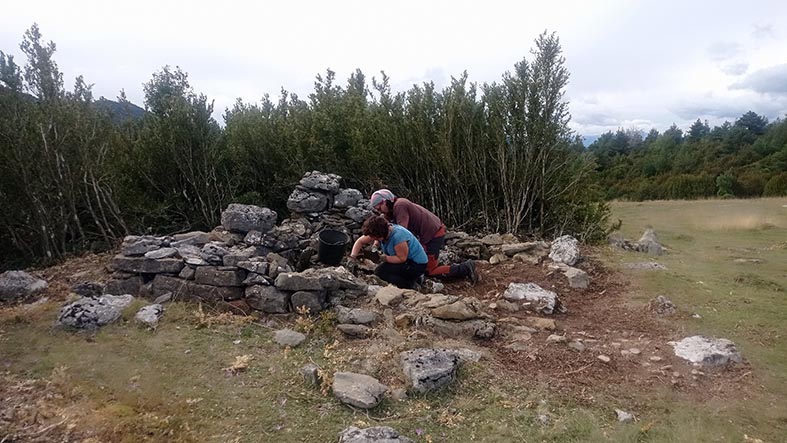 Colour photo of two people excavating inside a ruined stone-built structure.