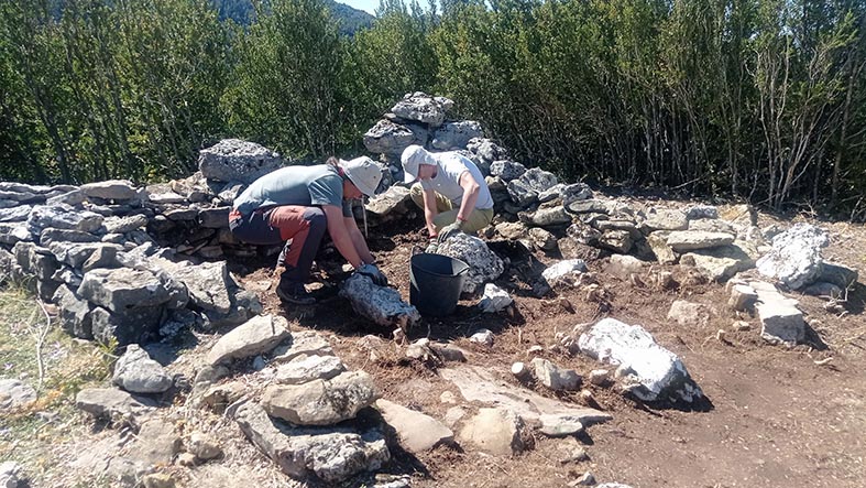Colour photo of two people excavating inside a ruined stone-built structure.