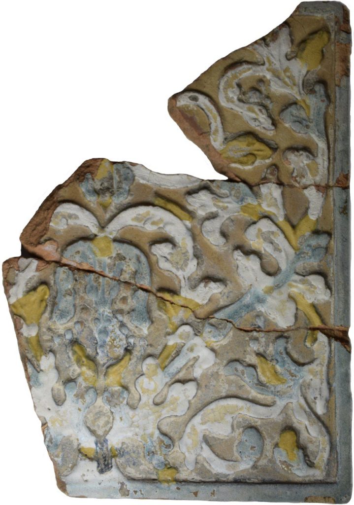 Colour photo of a floral patterned stove tile in black, grey, teal and yellow glazes.