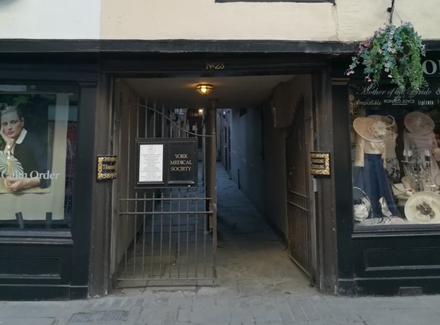 Colour photo of the passage leading from Stonegate, between two shop fronts and with an iron gate.