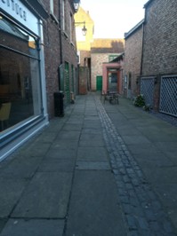 Colour photo of a broad alley laid to stone paving slabs.