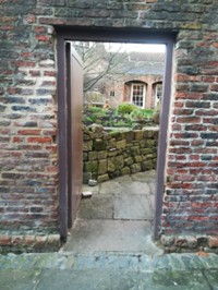 Colour photo of an open doorway in a brick wall leading into a garden.