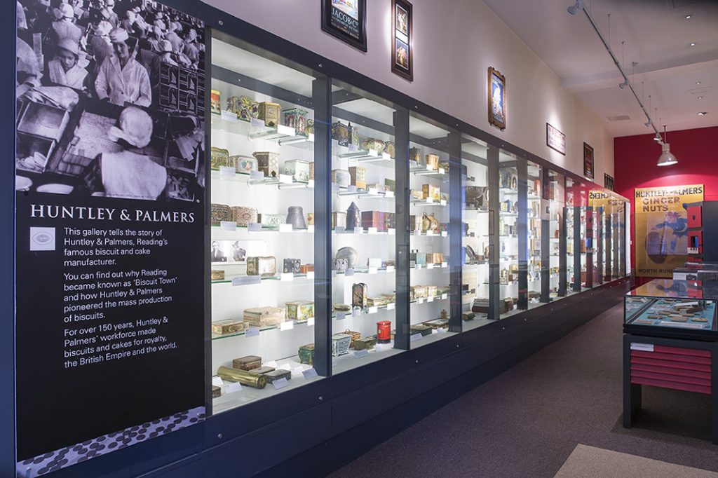 Colour photo of a museum gallery displaying hundreds of Huntley and Palmer biscuit tins in a long glass case.