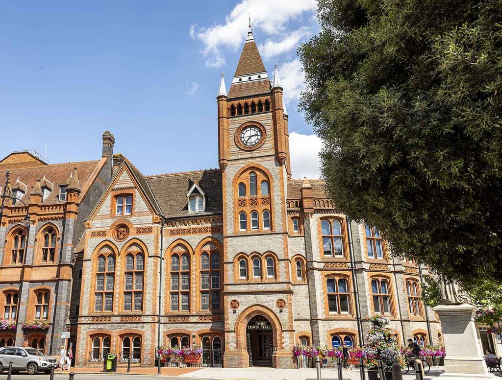 Colour photo of a grand Victorian Gothic red and grey brick building on a sunny day.