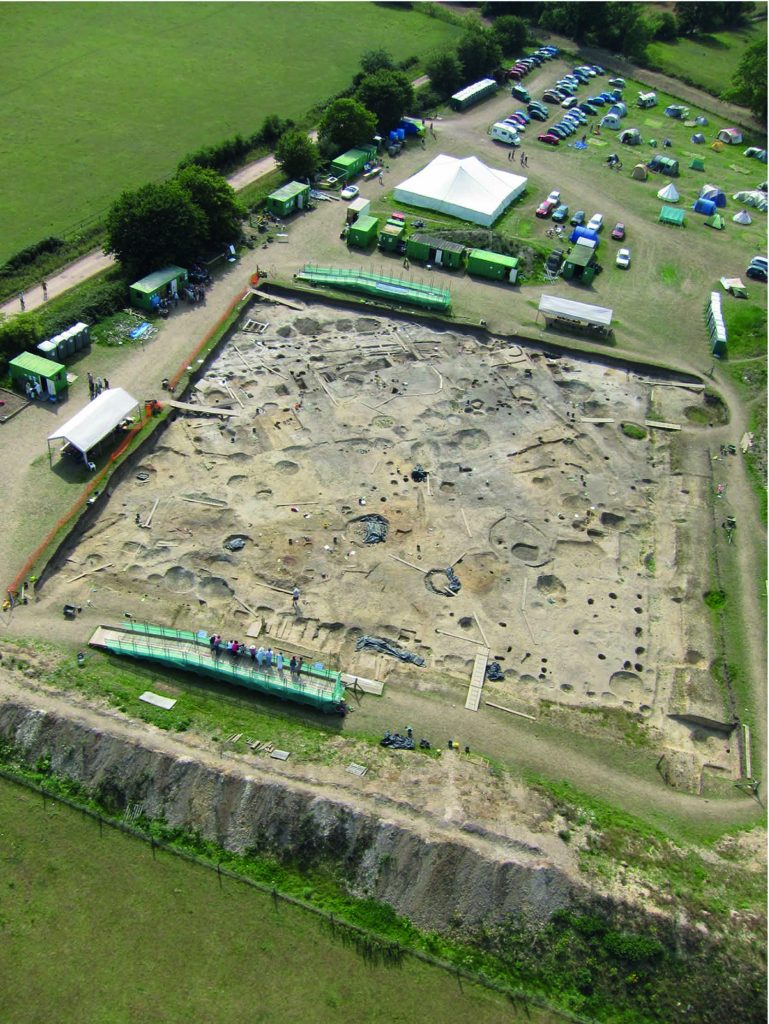 Colour oblique aerial photograph showing a stripped square area of ground under archaeological excavation.