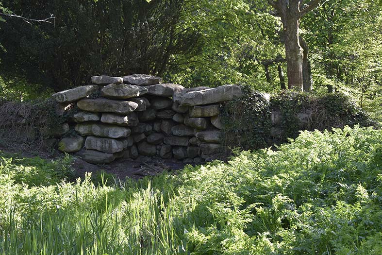 Colour photo of many gray boulders arranged to look like a cave or rock-shelter, in woodland
