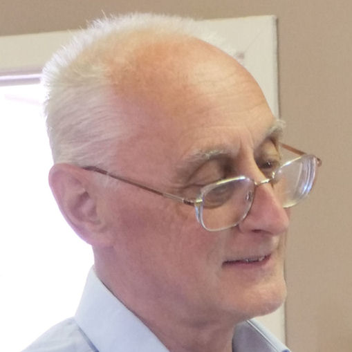 Colour head shot of a man with short white hair and wearing glasses, looking to the right.