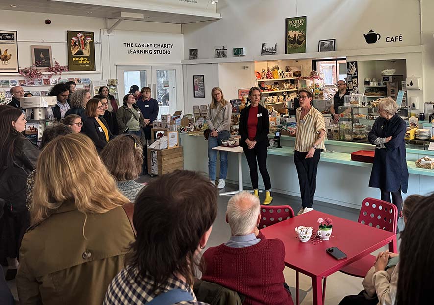A large group of people standing in a museum cafe listening to speeches.